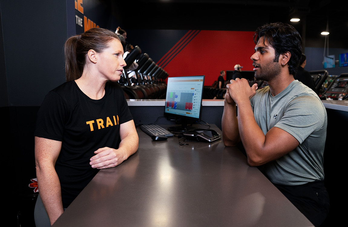 Crunch Signature personal trainer consulting with a member at the training desk with performance data on screen