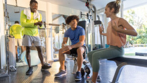 Experienced fitness coach mentoring a new trainer on the gym floor — first year coaching career advice