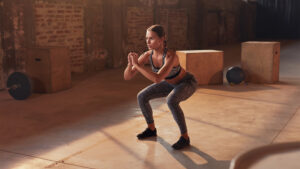 Personal trainer using a chair and resistance band to correct a client's squat form in a gym