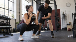 Personal trainer coaching a client through a goblet squat next to a chest-supported row bench in a gym