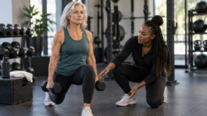 Fitness coach guiding an older adult client through a supervised strength training exercise.