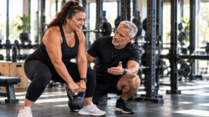 Three fitness coaches of different ages and body types coaching clients on a busy gym floor.